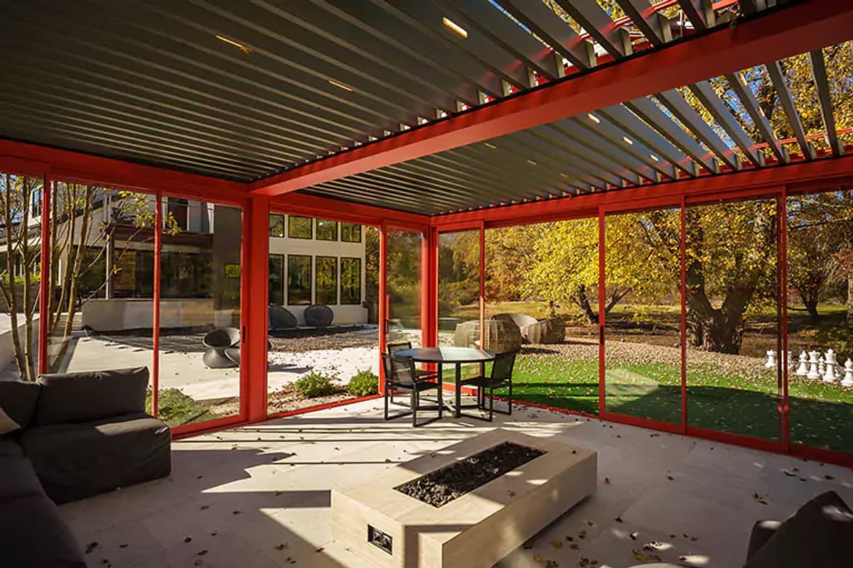 Red-framed louvred pergola with glass side panels and a fire table