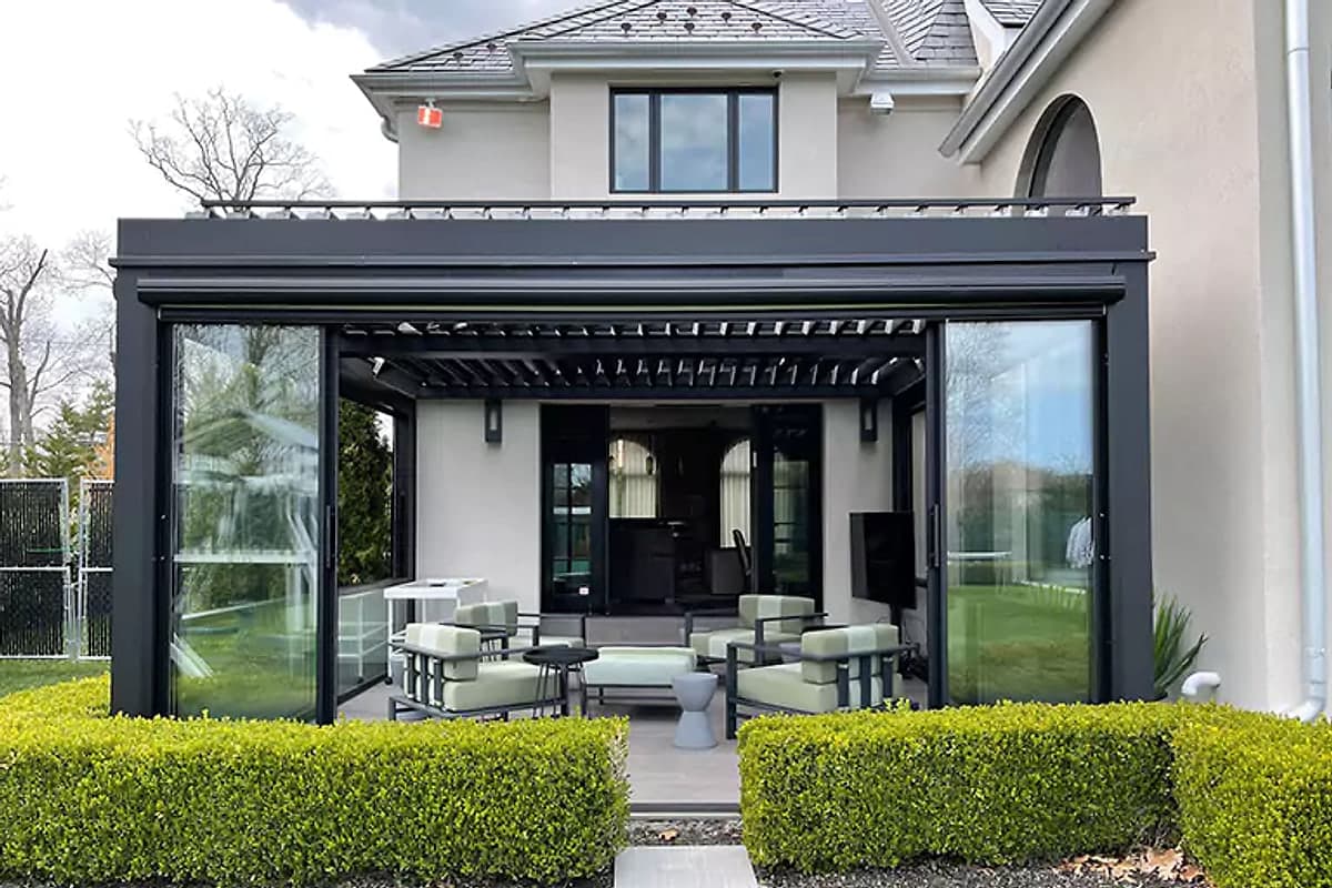 Louvred pergola with sliding glass doors and lounge seating in front of a modern house